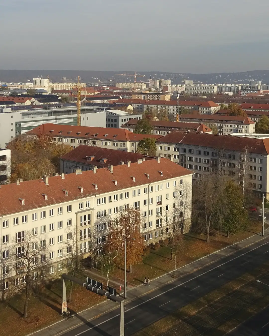 Blick von oben über die Pirnaische Vorstadt: helle Wohnblöcke mit roten Dächern an einer breiten Straße mit Herbstbäumen, dahinter weitere Stadtteile und Hügel unter blauem Himmel