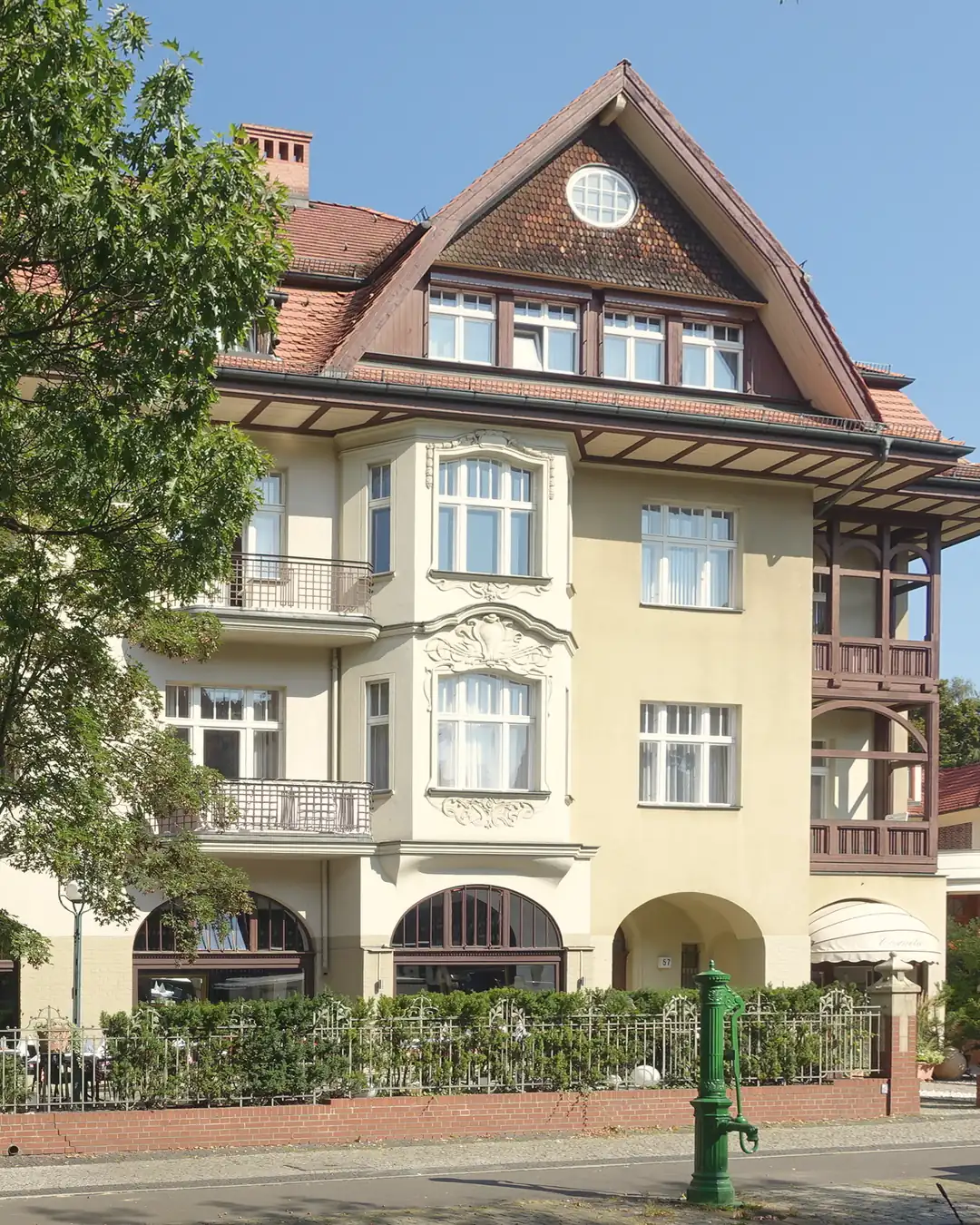 Ein Mietshaus mit Ziergiebel und Balkonen in der Beerenstraße in Zehlendorf in der Sonne, davor Bäume